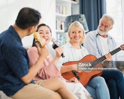 Group of positive seniors European and Asian are singing with playing a guitar at retirement home. Retired people are playing music which fun to enjoying and smiling felling happy. life at home.