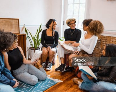 Group of teenage girls reading books together sitting on the living room’s floor.