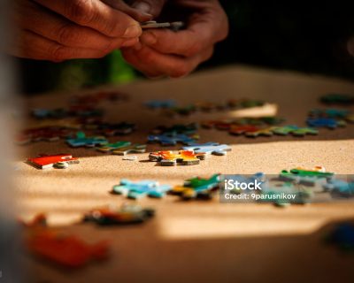 Elements of the puzzle are laid out on a table. Man hands fold puzzles.