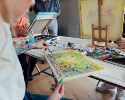 Close up of an unrecognisable small group of friends attending an art class at an art studio in a home in Horsely, Northumberland, England. Guided by an experienced art instructor they are drawing oil pastel drawings and painting on canvases.