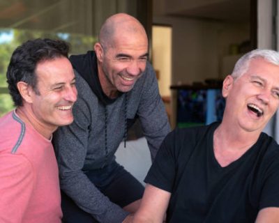 Three older male friends smiling and hugging, enjoying a day together.