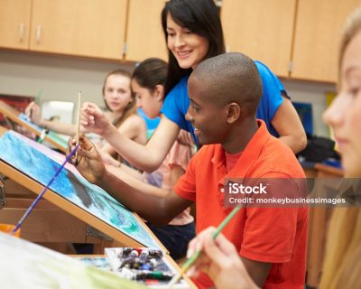 Male Pupil In High School Art Class With Teacher Painting