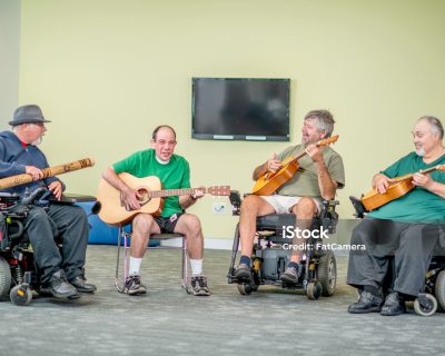 A group of disabled adult males are sitting and happily playing music together.